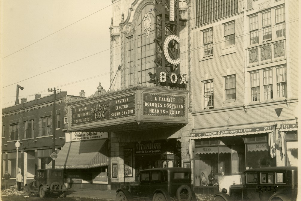 Vintage photograph from around 1929 of Music Box Theatre with a dirt street and cars from the 1920s. The marquee mentions "A Talkie, Dolores Costello, Hearts in Exile"