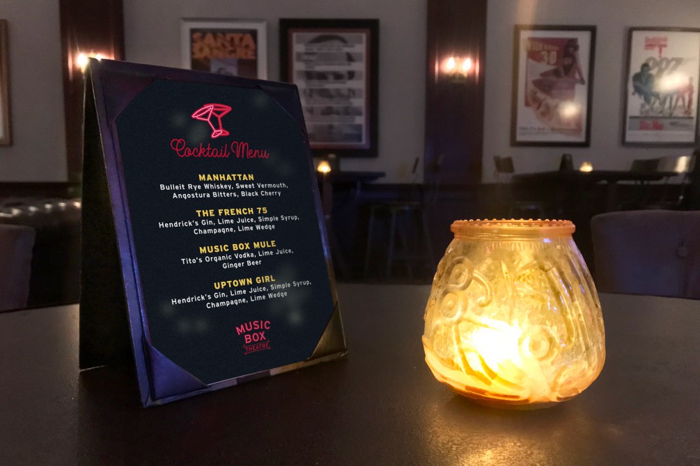 Cocktail menu next to a lit candle on a tabletop in the Music Box Lounge.