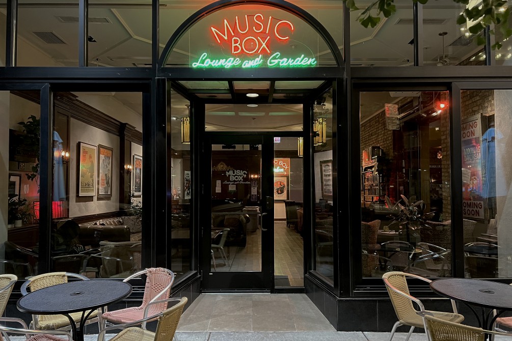 Exterior image of the Music Box Lounge & Garden looking in through the glass facade and neon lights.
